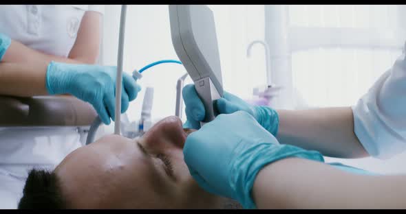 A Patient Lies in a Dental Chair While a Doctor Examines His Teeth Using Camera