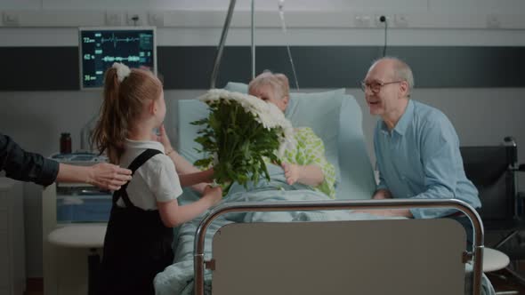 Little Girl Running to Hug and Give Flowers to Aged Patient in Hospital Ward Bed