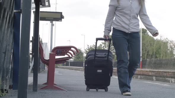 Woman wheels suitcase on train platform towards camera wide shot