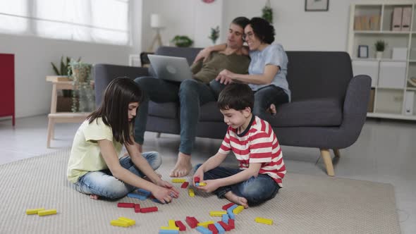 Kids Playing on the Floor While Parents Using Laptop in the Living Room at Home
