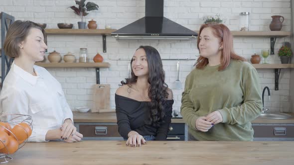 Three Young Positive Caucasian Women Chatting and Laughing in Kitchen Indoors