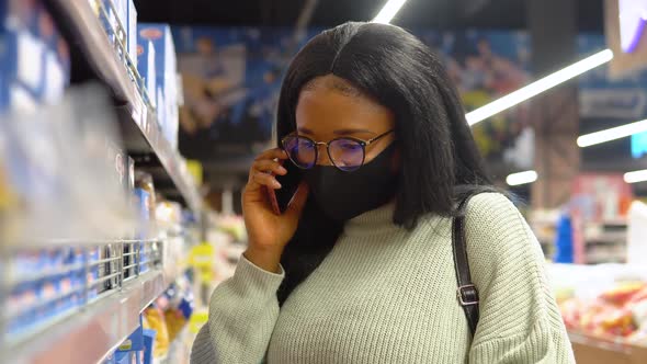 The Girl in a Mask Chooses Products on the Shelves in the Supermarket