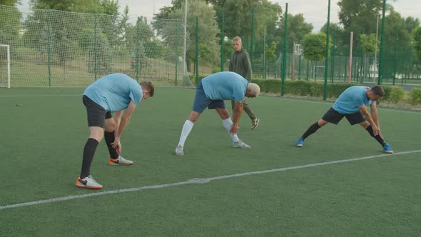 Soccer Players Stretching Performing Forward Bend Exercise Outdoors