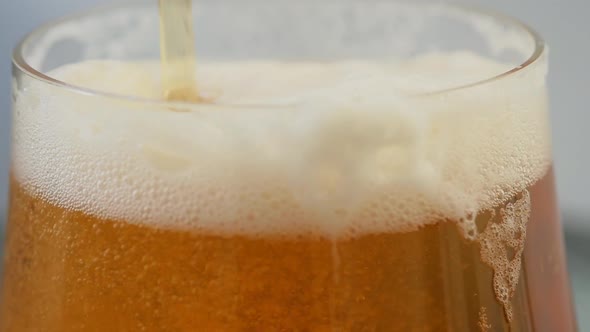 Slow motion close up of a lager beer foaming up after pour in glass. As the beer continues to fill u