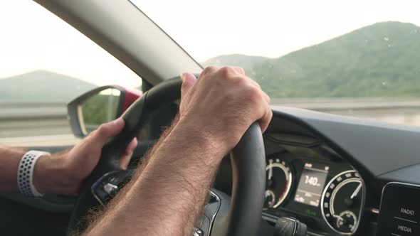 Man Hands Hold Steering Wheel of Car Driving Past Mountains