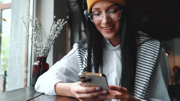 Handsome young brunette woman wearing hat and eyeglasses texting by phone