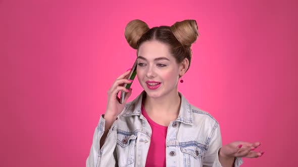 Teenager Speaks on the Phone with Her Sibling. Pink Background. Slow Motion