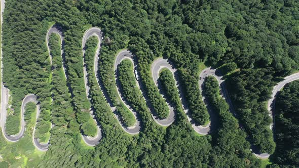 Aerial view of cars driving along scenic curvy serpentine road in the mountains by drone
