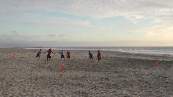 A group of guys playing flag football on the beach.