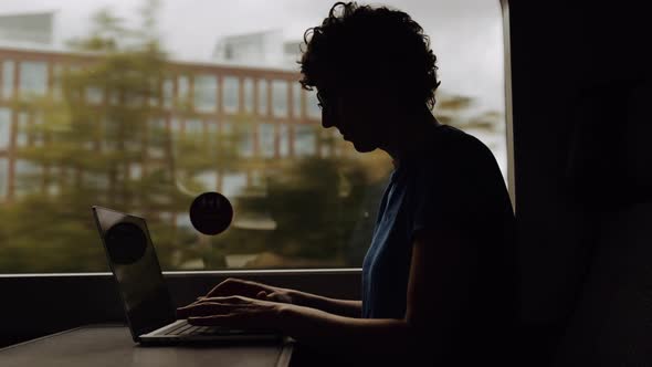 Silhouette of a Woman in Glasses Working on a Laptop While Going By Train