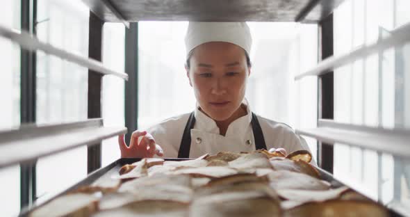 Animation of happy asian female baker checking freshly prepared rolls