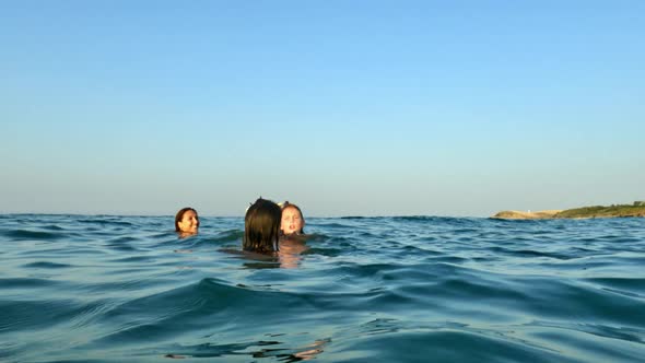 Girls and child relax bathing offshore with motorboat floating in background. Slow-motion