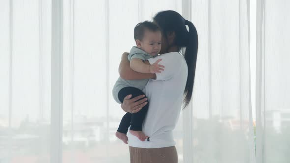 Young asian mother holding little baby girl and walking together in the bedroom at home.
