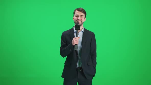 Male Reporter Looks Into the Camera and Speaks Into a Microphone on a Green Background a Template