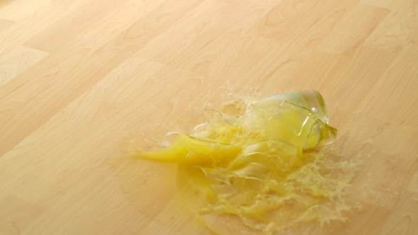 Dropping Glass of orange juice and breaking on wooden floor, Slow Motion