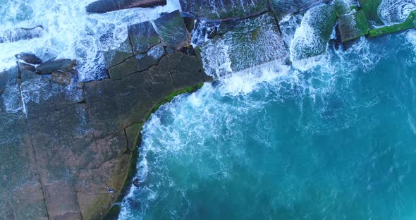 Scenic view of stone rocky jetty in blue green ocean sea water and waves crashing onshore, above ris