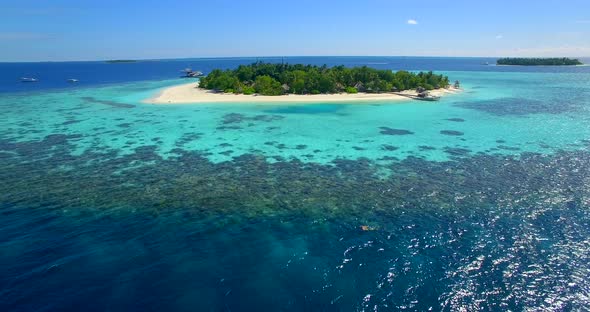 Aerial drone view of a man and woman couple snorkeling over a coral reef of a tropical island.