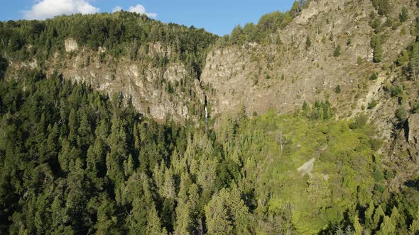 Aerial dolly in flying above cypress woods and Corbata Blanca thaw waterfall between mountains, Pata