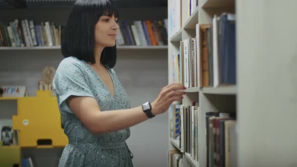 Happy Woman Reads a Book in the Library Chooses Books From the Shelf