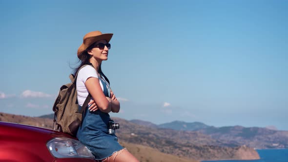 Relaxed Travel Backpacker Woman Admiring Beautiful Seascape Sitting on Car Bonnet Side View