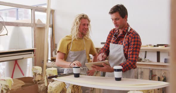 Two Caucasian male surfboard makers standing and working on projects using a tablet