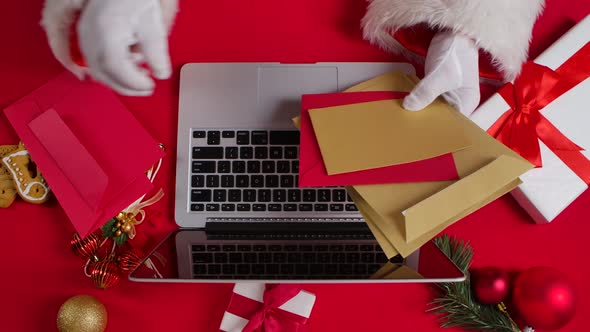 Top View Santa Hands in White Gloves are Typing on Keyboard Laptop By Red New Year Decorated Table