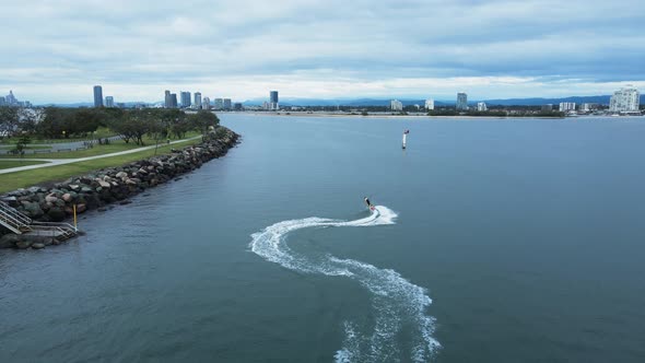 A jet board carves through the glassy waters along a city harbor break wall. Drone view