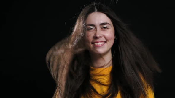 Portrait of a Young Smiling Woman Posing on a Black Background and Her Hair From Below Blows the Air