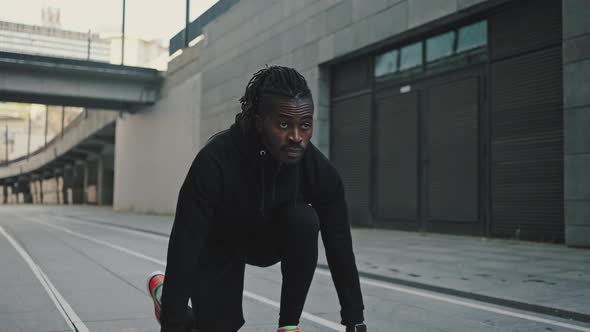 Zoom Out Portrait of Focused African American Guy Standing in Start Position and Run in Urban Area