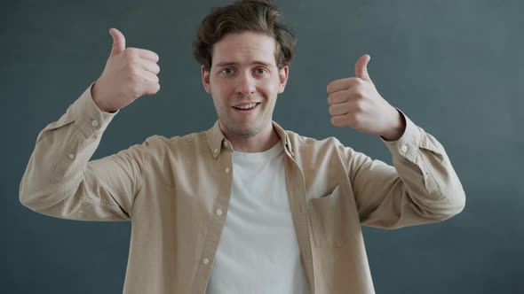 Portrait of Young Man Showing Thumbsup Then Thumbsdown Hand Gesture and Looking at Camera with