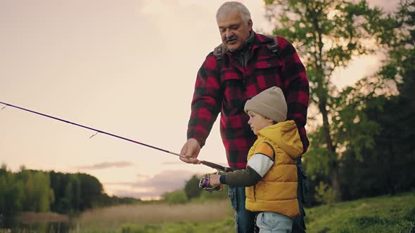 Child Boy is Fishing in Lake Grandfather or Dad is Helping Him Happy Family is Resting in Nature