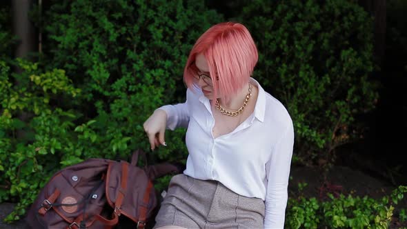 A Student with Pink Hair Puts a Backpack on the Parapet and Takes Out a Mobile Phone From Her Pocket