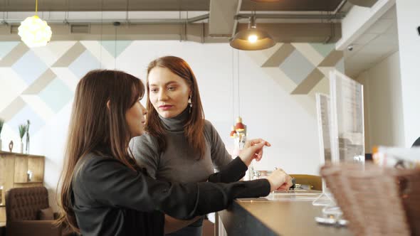 Two Women Discuss the Menu and Choose Food in a Cafe Standing at the Bar Counter