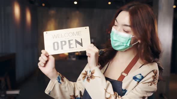 Business owner attractive young asian woman in apron hanging we're open sign.