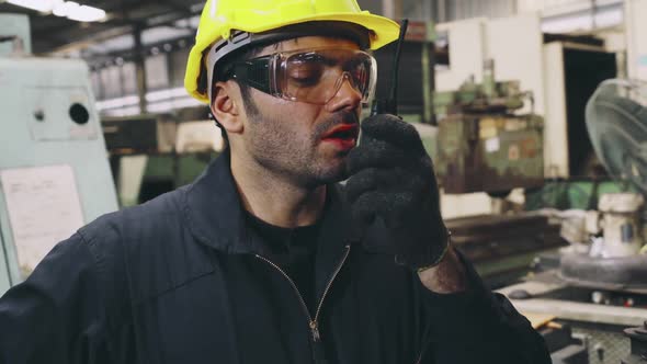 Factory Worker Talking on Portable Radio While Inspecting Machinery Parts