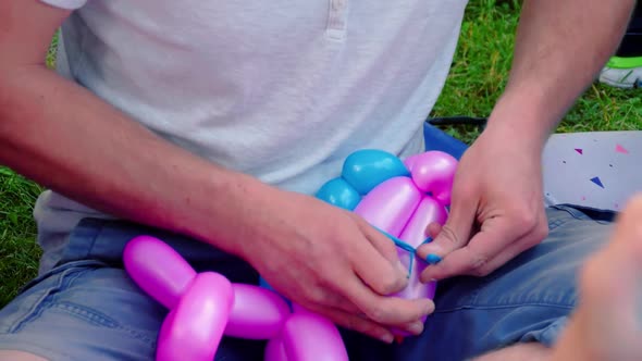 Balloon artist tying balloons in park. Inflating a pink balloon with plastic pump.  Concept of fun,