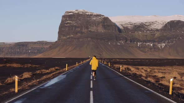 Back View of a Man Running Along an Empty Asphalt Mountain Road in Iceland