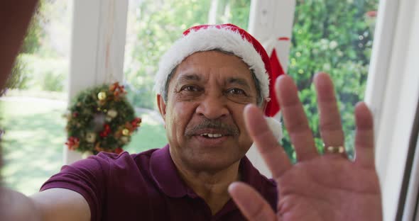 Portrait of happy senior man in santa hat waving hand during christmas video call