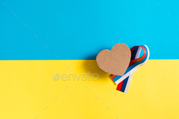 Cardboard heart and ribbon of the Russian flag on the background of the Ukrainian flag.