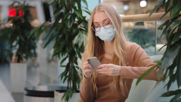 Caucasian Blonde Woman Wearing Medical Mask in Shopping Center Mall Company Looking at Phone Screen