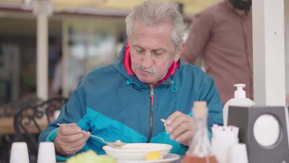 An old man drinks soup and eats bread at restaurant, a traditional soup