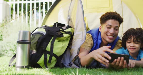 Happy biracial man and his son using smartphone in garden