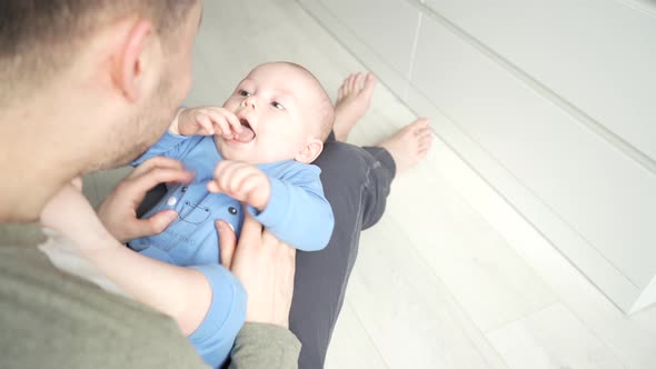 Father Plays with a Smiling Baby Son Lying on Knees at Home Together