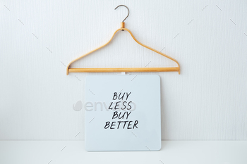 conomy, Sustainable fashion concept with wooden clothes hangers and text Buy less, buy better.