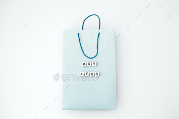 conomy, Minimalism, Sustainable fashion concept with empty paper shopping bag and clothes hangers and text Buy less