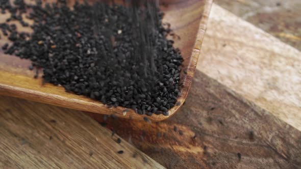 Black sesame seeds on a rustic wooden surface. Falling in slow motion. Close up