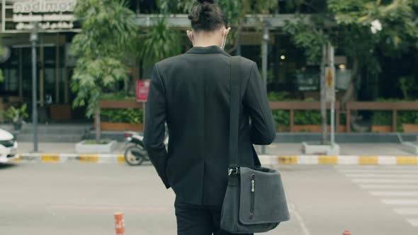 Asian businessman casual dress carrying a shoulder bag while standing in the street.