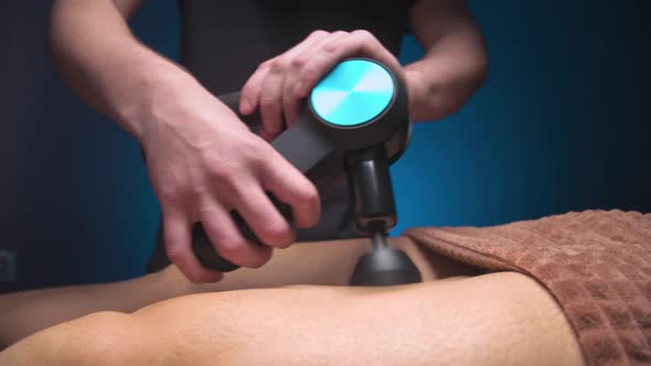Male Masseur Doing Massage Exercises on the Thighs with the Help of a Percussion Vibro Massager to a