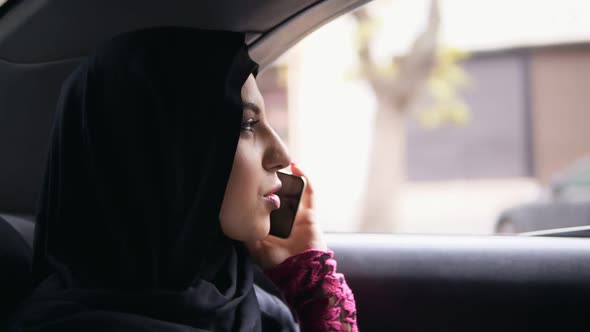 Young Attractive Woman Wearing Hijab Sitting on the Back Seat in Taxi and Talking on the Phone