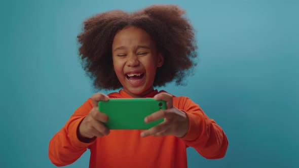 Cheerful African American girl playing video game using mobile phone game application